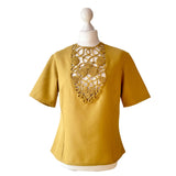 Mustard yellow vintage blouse with intricate cut-out rouleaux design on a mannequin against a white background