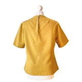 Mustard yellow vintage blouse on a mannequin against a white background