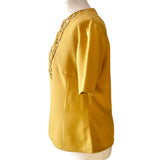 Vintage mustard yellow blouse on mannequin against a white background