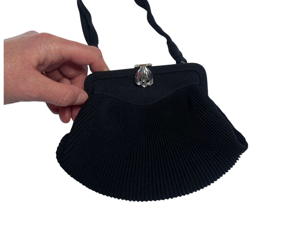 Black pleated vintage 1960s RFC handbag with a decorative clasp held by a hand on a white background