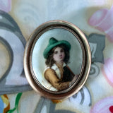 Antique brooch with a portrait of a  Hand Painted Victorian Tyrolean boy in a green hat on a fabric background.