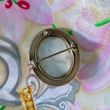 Antique brass framed oval brooch on pink fabric 
