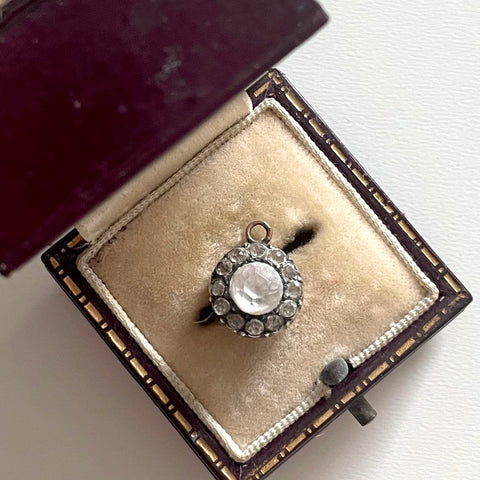 Tiny 1700s antique colourless paste round pendant with central stone surrounded by 12 smaller ones in a velvet-lined box on a white background